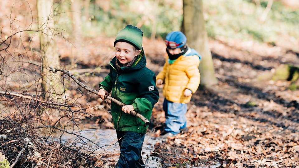 Jungen im Kita-Alter spielen mit Stöcken im Wald. 