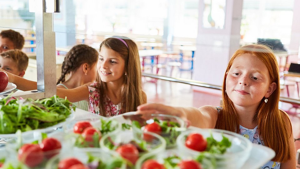 Schulmädchen bedienen sich in einer Mensa an der Salatbar. 