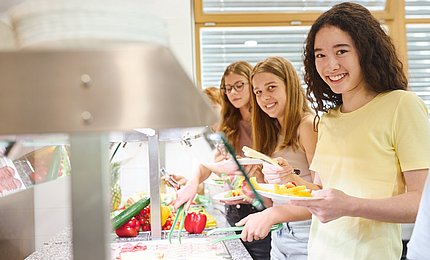 Schulmädchen bedienen sich an einer Salatbar in der Mensa.   
