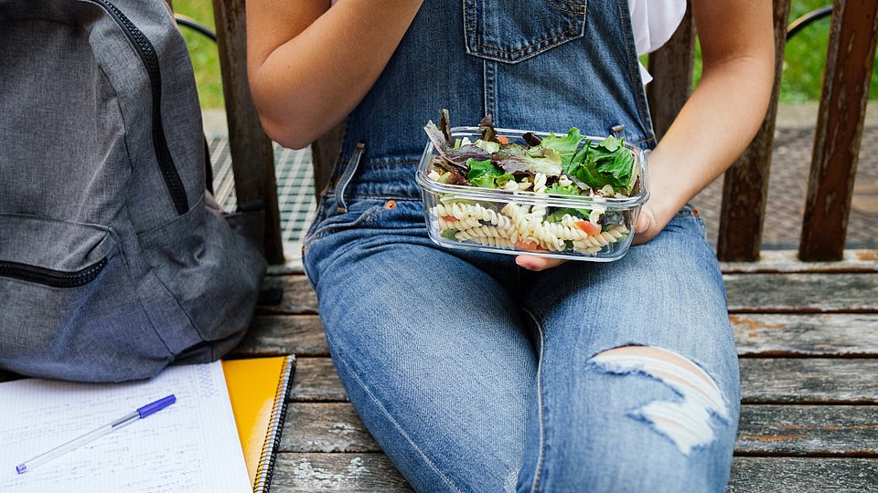 Jugendliche Schülerin hält mitgebrachtes Schulessen auf dem Schoß.  