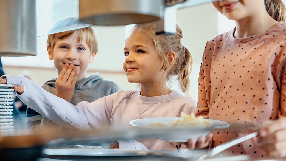 Schulkinder stehen in der Mensa und bedienen sich an der Nudel-Bar. 