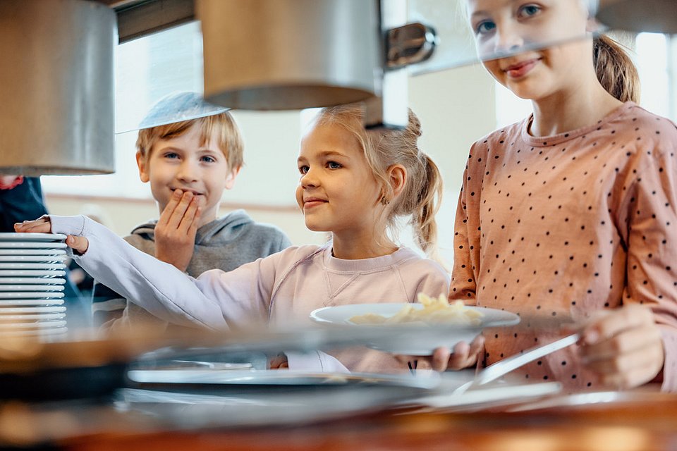 Schulkinder stehen in der Mensa und bedienen sich an der Nudel-Bar. 