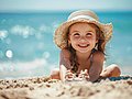 Kleines Mädchen mit Strohhut liegt am Sandstrand.