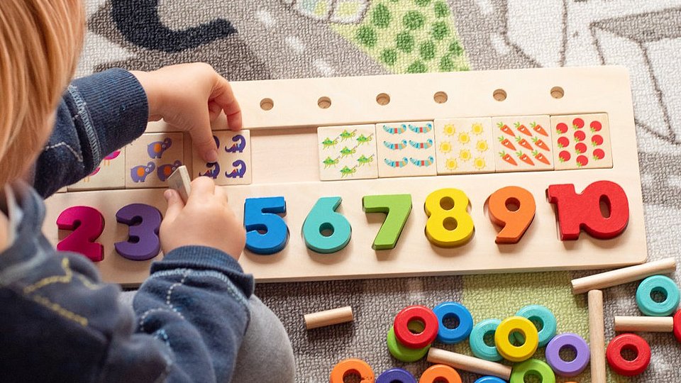Ein Kind spielt mit einem Puzzle aus Holz, wobei Zahlen und Muster einsortiert werden müssen. 