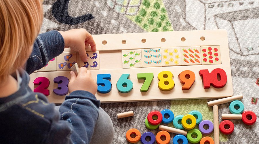 Ein Kind spielt mit einem Puzzle aus Holz, wobei Zahlen und Muster einsortiert werden müssen. 