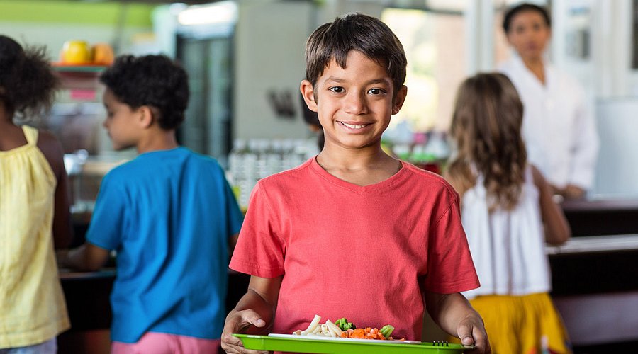 Schulkind in der Schulkantine, auf dem Tablett steht ein Teller mit Schulessen. 