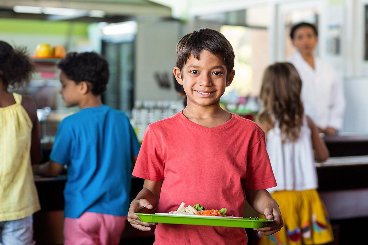 Schulkind in der Schulkantine, auf dem Tablett steht ein Teller mit Schulessen. 