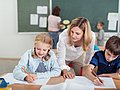 Die Szene zeigt eine Interaktion zwischen Lehrerin und zwei Grundschulkindern. 