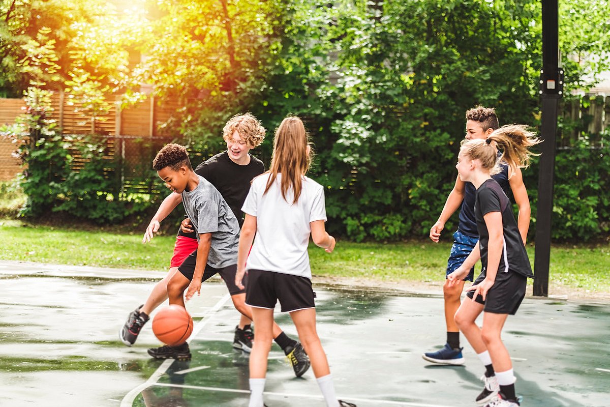 Jugendliche Mädchen und Jungen spielen Basketball.