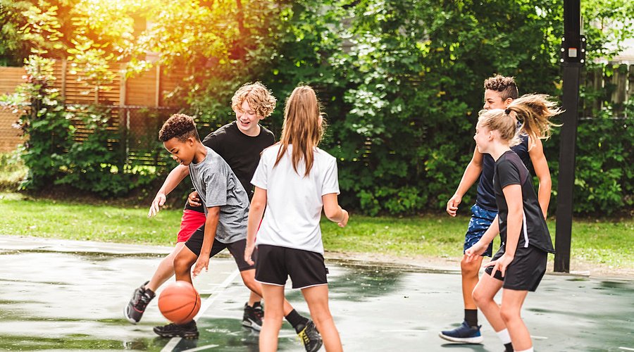 Jugendliche Mädchen und Jungen spielen Basketball.