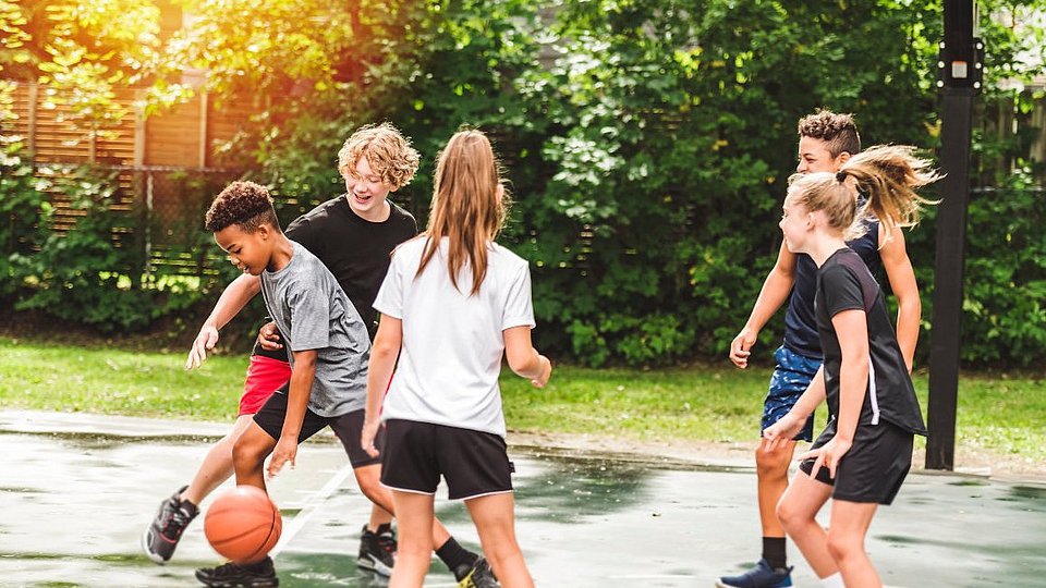 Jugendliche Mädchen und Jungen spielen Basketball.