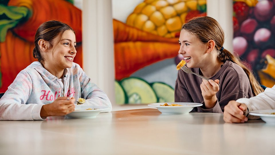Schulmädchen sitzen in der Mensa am Tisch und unterhalten sich. 