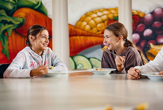 Schulmädchen sitzen in der Mensa am Tisch und unterhalten sich. 