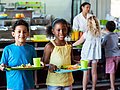 Schulkinder in der Mensa halten ihr Tablett mit dem Mittagessen.