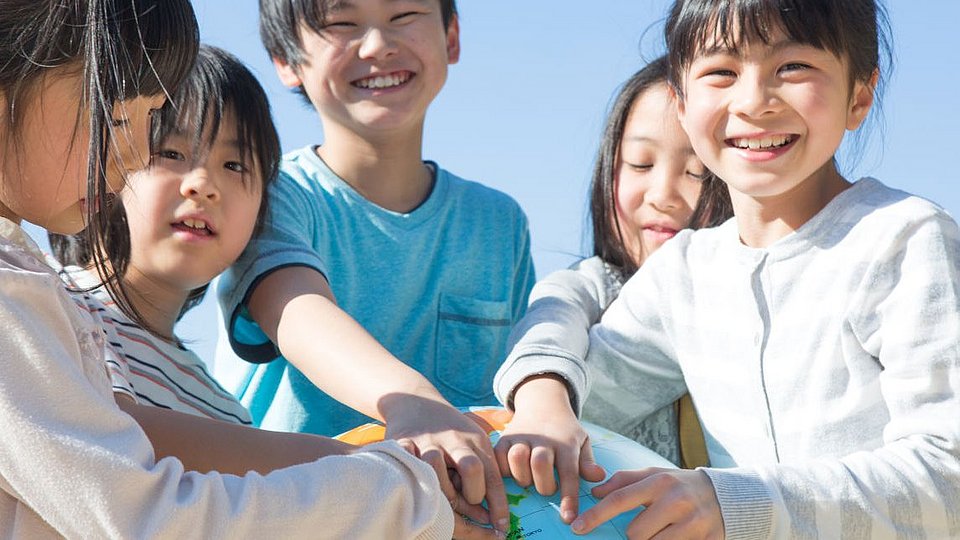 Schulkinder in Japan zeigen auf einem Globus, wo ihr Land liegt.