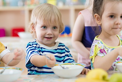 Kita-Kind rührt mit einem Löffel in seiner Schale.