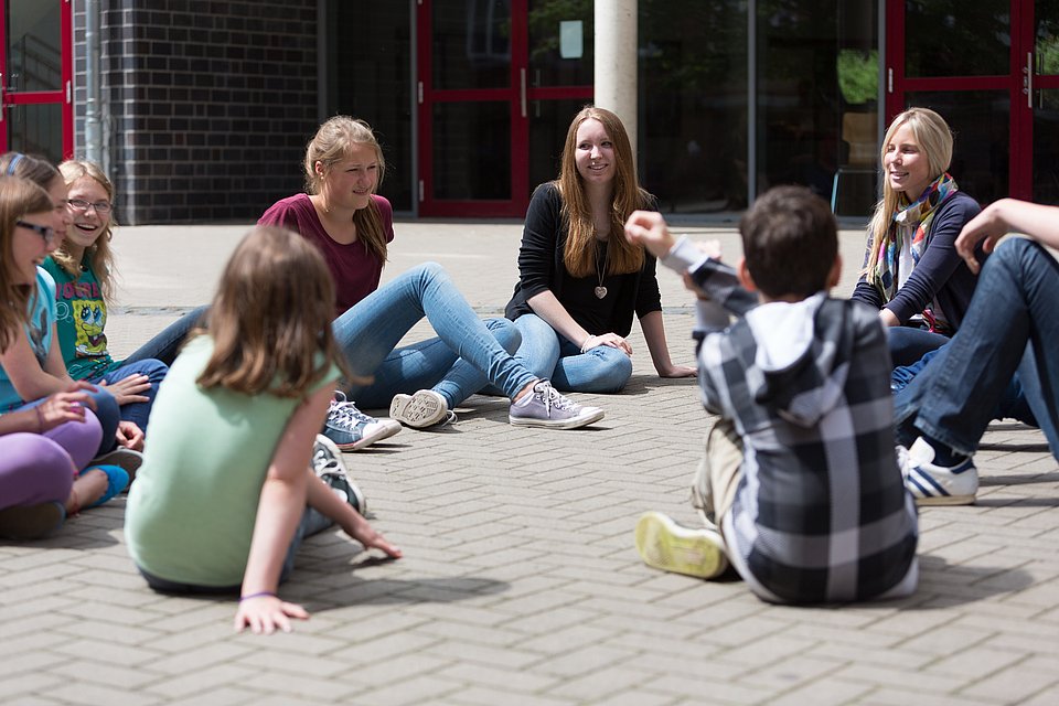 Schülerinnen und Schüler sitzen im Kreis auf dem Schulhof und diskutieren.