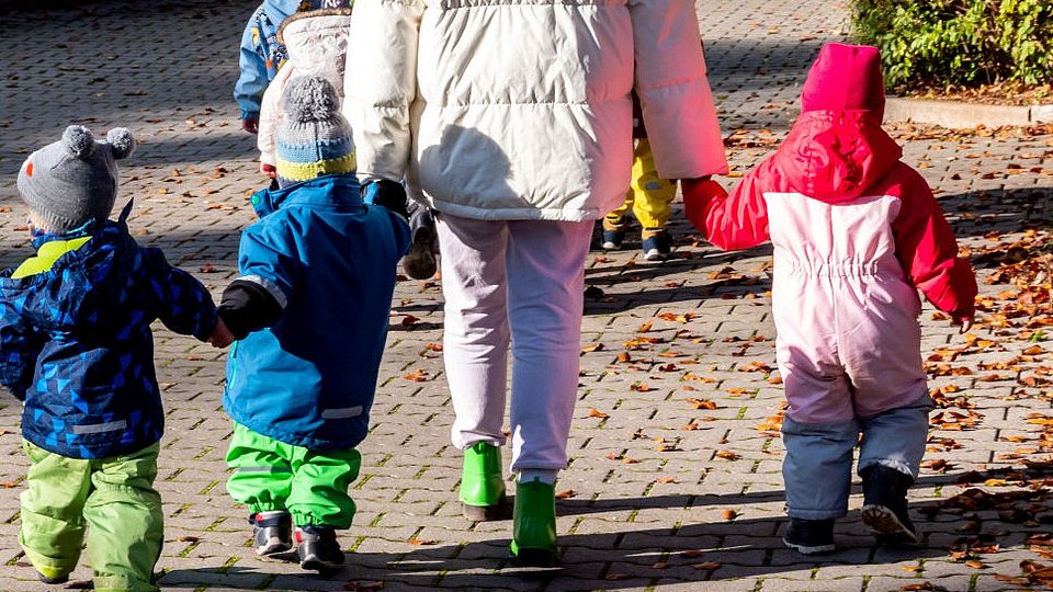 Erzieherin macht mit kleinen Kindern einen Herbstspaziergang.