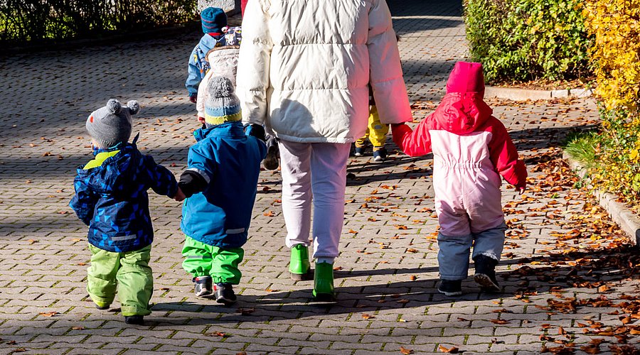 Erzieherin macht mit kleinen Kindern einen Herbstspaziergang.