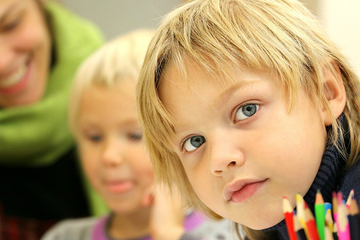 Ein Junge im Grundschulalter sitzt mit Gleichaltrigen an einem Tisch, vor ihm eine Stiftebox.