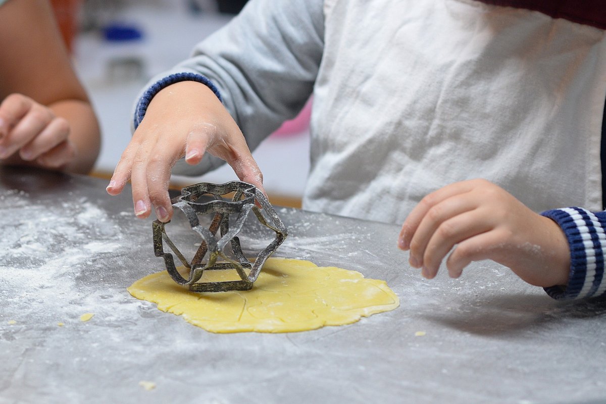 Das Foto zeigt ein kleineres Kind mit Schürze, das Plätzchenteig aussticht.