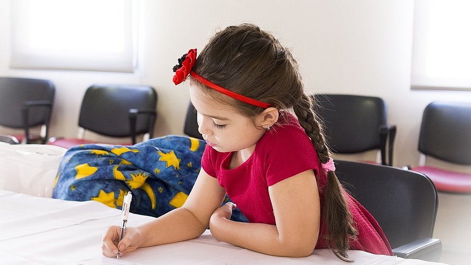 Schulmädchen sitzt am Tisch und schreibt in ein Schulheft. 