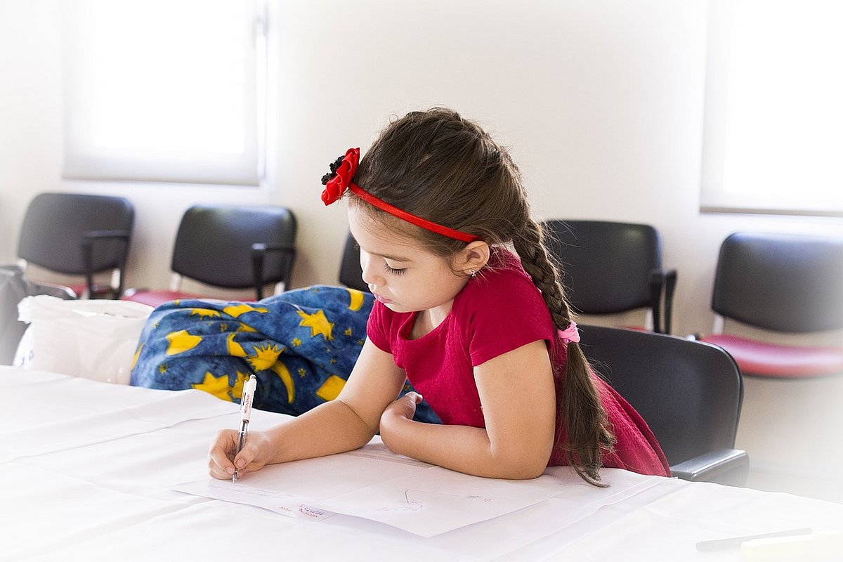 Schulmädchen sitzt am Tisch und schreibt in ein Schulheft. 