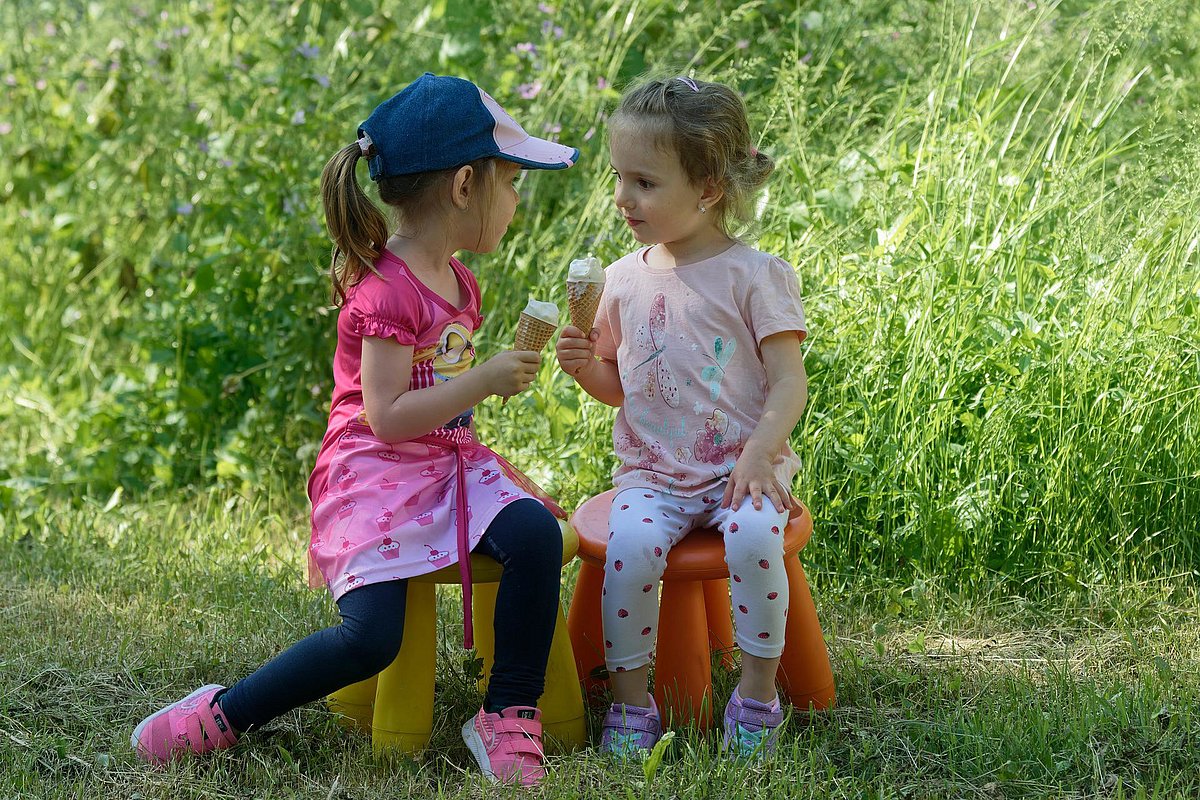 Zwei Kita-Mädchen sitzen im Garten und essen ein Eis. 