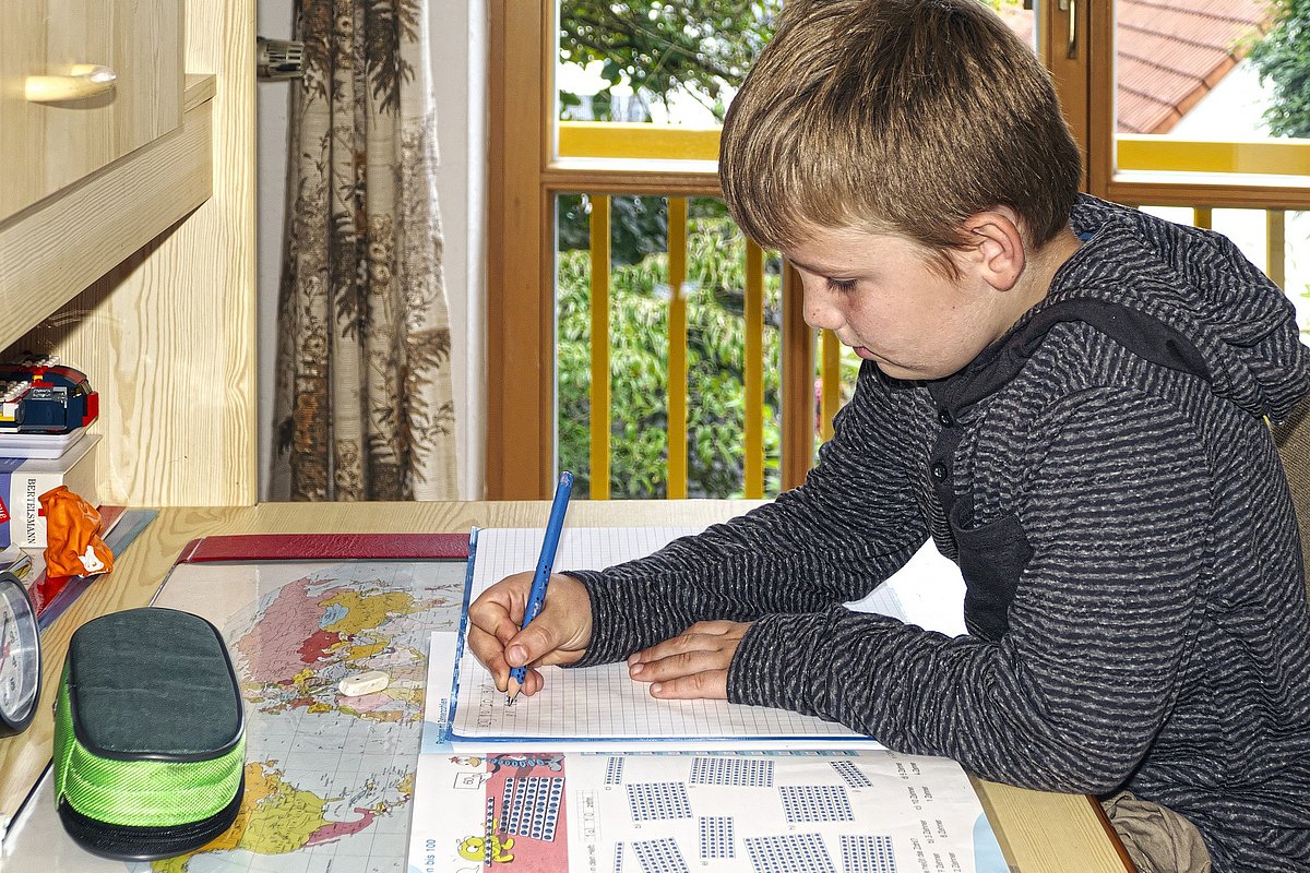 Ein jugendlicher Junge sitzt an seinem Schreibtisch und macht seine Hausaufgaben.