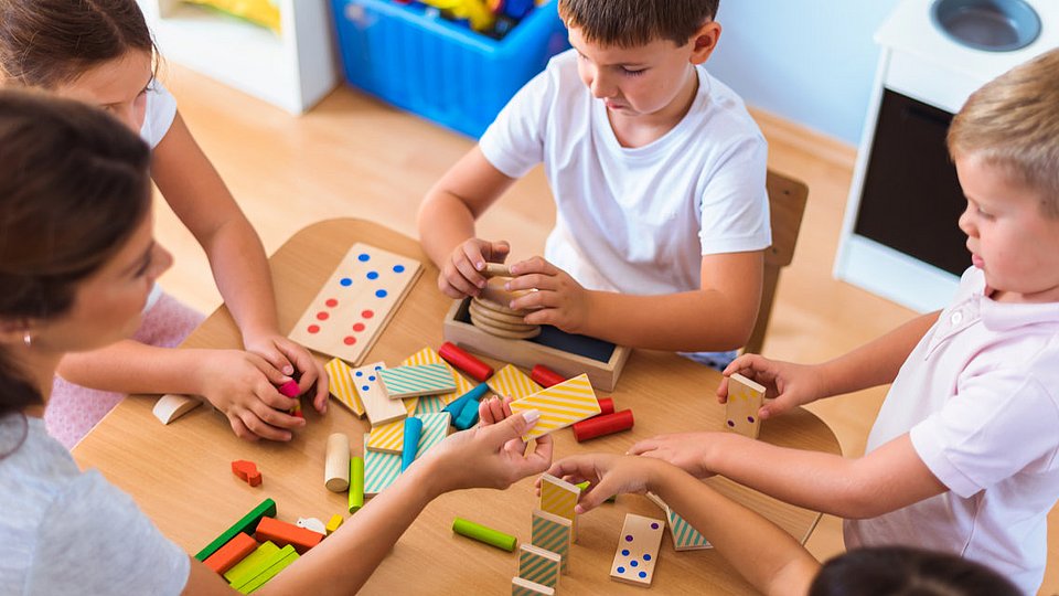 Eine pädagogische Fachkraft spielt mit Kita-Kindern. 