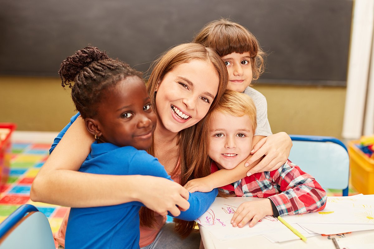 Eine pädagogische Fachkraft umarmt mehrere Kita-Kinder. 