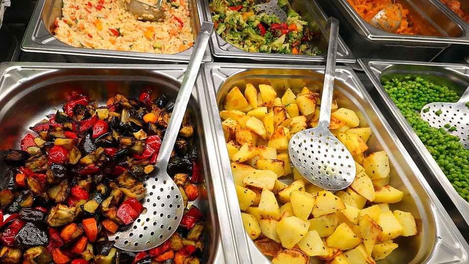 Mehrere Gastro-Norm Behälter in einer Ausgabetheke mit vegetarischem Essen. 